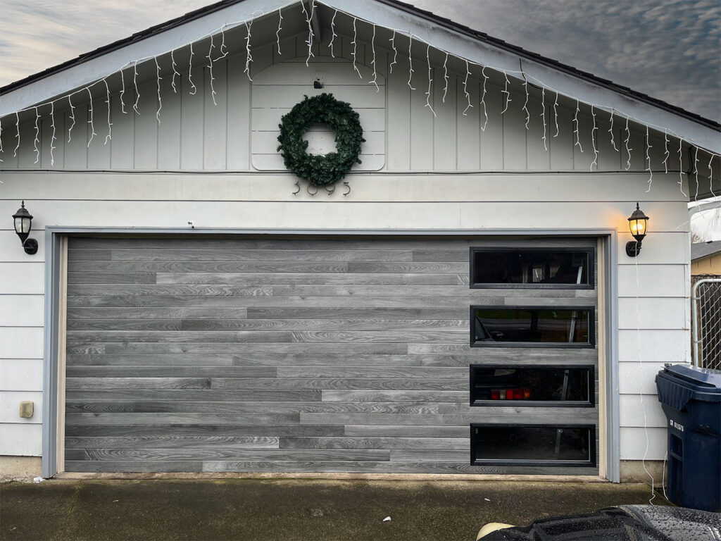 Gray wood-look garage door with a holiday wreath on a Eugene home